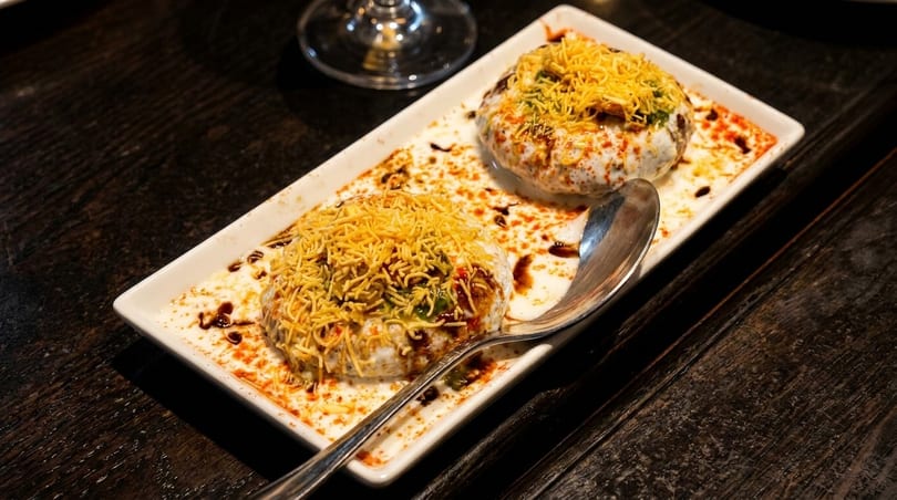 Two servings of Indian dahi vada, topped with sev and sauces, on a white rectangular plate.