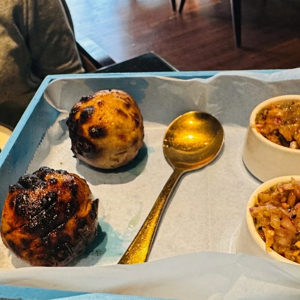 Two charred bread rolls, a golden spoon, and two bowls of chutney on a blue tray.
