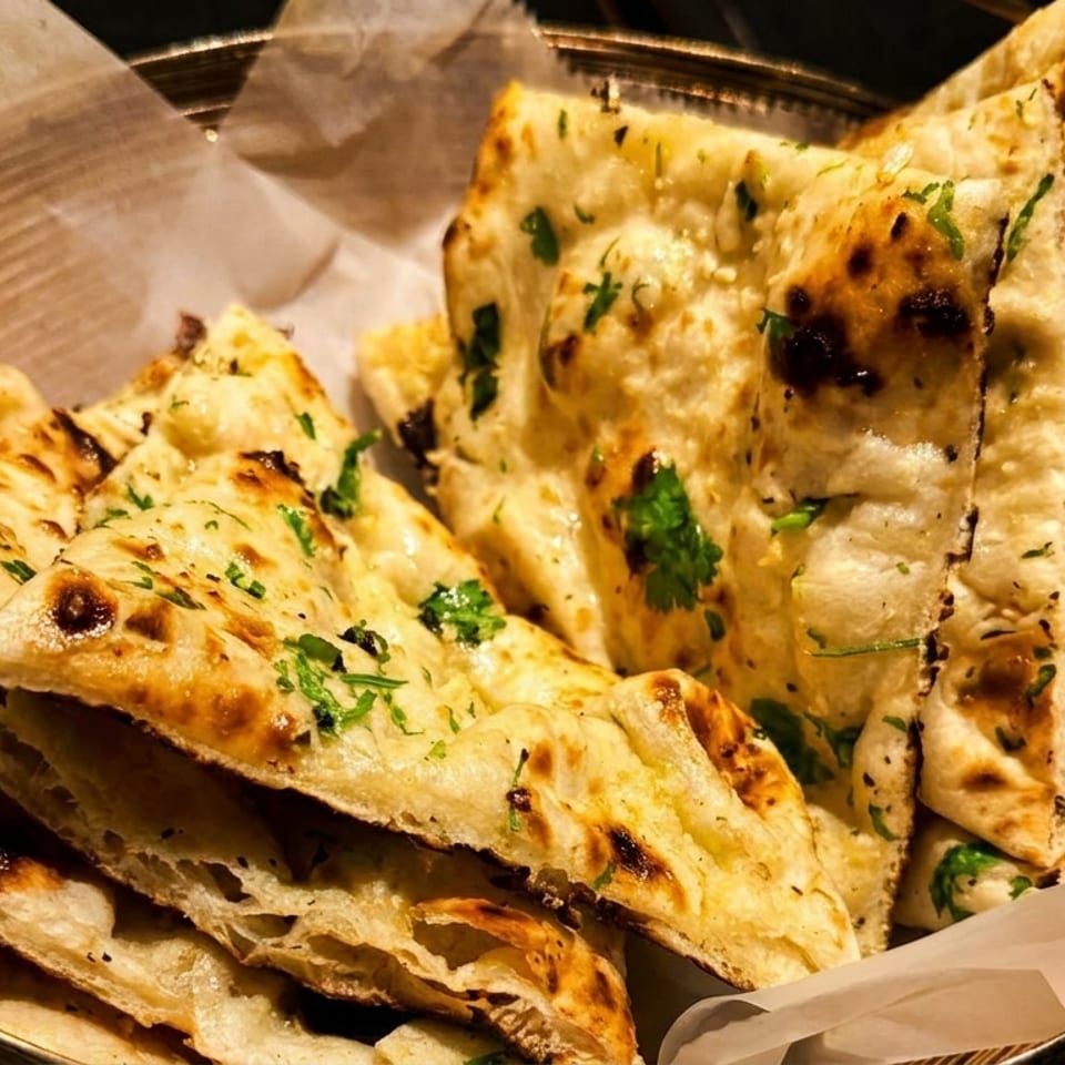 Basket of warm, golden-brown naan bread with cilantro, served with a side of curry.