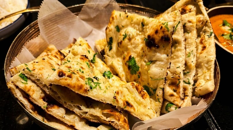 Basket of warm, golden-brown naan bread with cilantro, served with a side of curry.