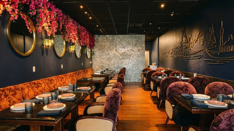Elegant restaurant interior with dark walls, floral decor, and set tables with plush seating.